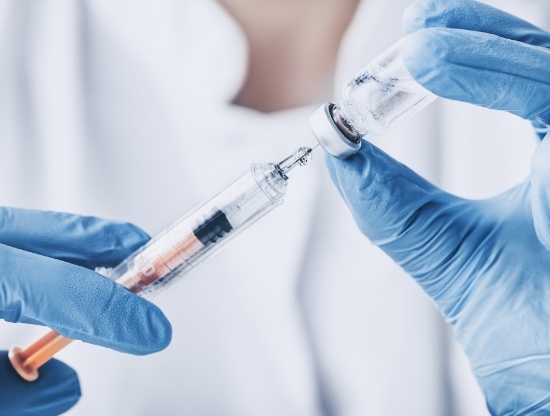 Dentist drawing syringe from vial of clear liquid