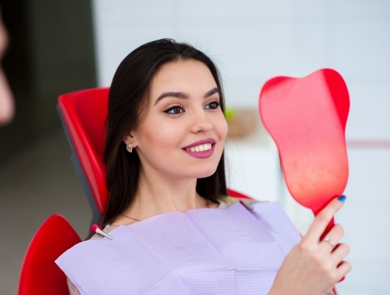 Dental patient looking at her smile in mirror after restorative dentistry in Rocky Hill